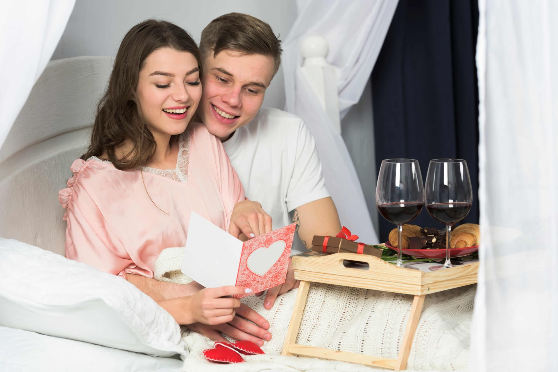 Jeune couple lisant une carte de vœux au lit